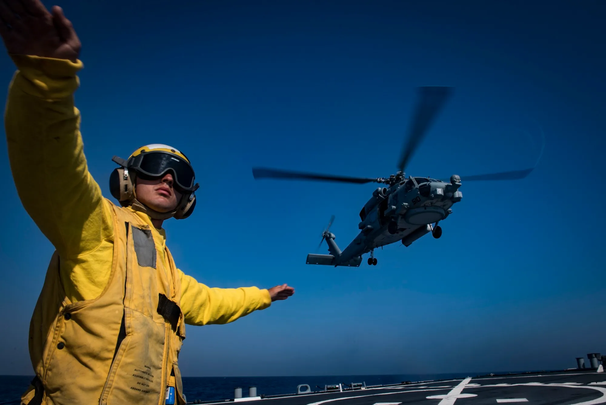 Flight-deck crewman signals an MH-60R Seahawk in over the deck