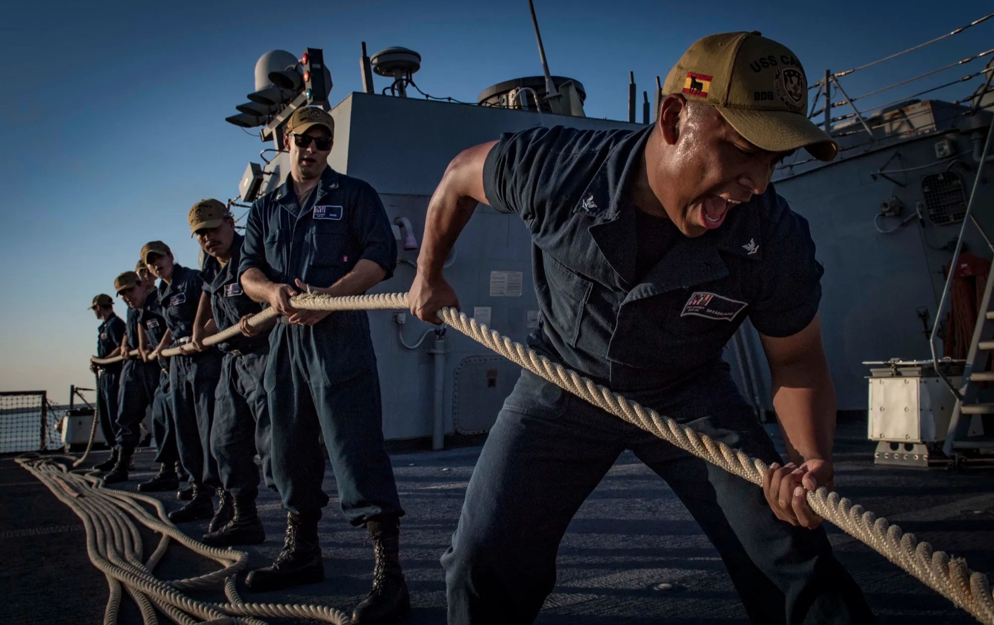USS Carney sailors heave a mooring line at golden hour