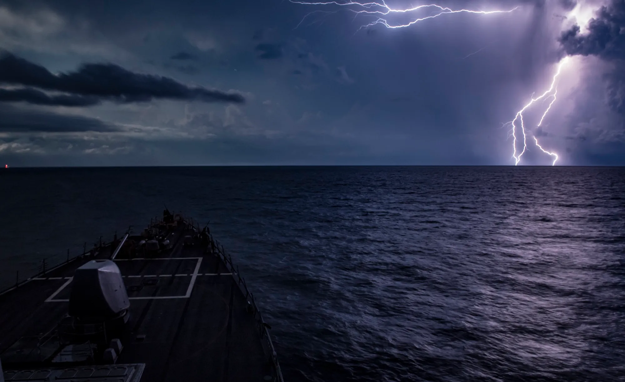 Lightning strikes the horizon off a destroyer’s bow at night
